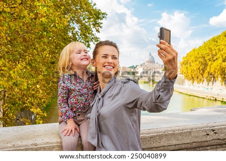 Happy mother and baby girl making selfie on bridge ponte umberto I with view on basilica di san pietro