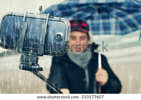 a young man taking a self-portrait with a selfie-stick under the rain
