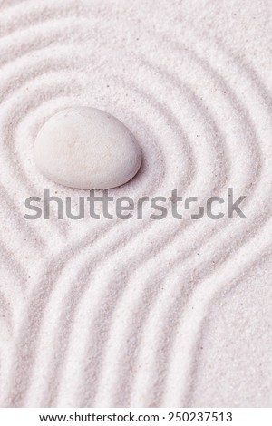 Zen garden with a silk white stone with wave patterns in the sand surrounding the stone