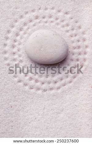 Zen garden with a relaxing beige stone with small dots in the sand surrounding the stone