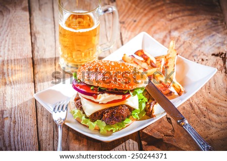 Delicious cheeseburger and french fries on a white plate on a wooden rustic table.