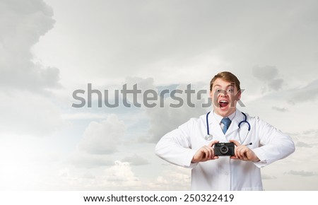 Funny young doctor with photo camera screaming emotionally