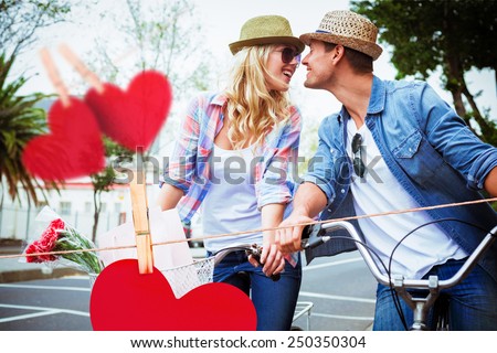 Hip young couple on a bike ride against hearts hanging on a line