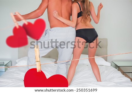 Low section of a semi dressed couple on bed against hearts hanging on a line