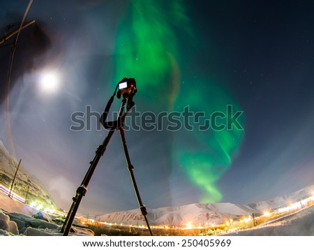 DSLR Camera on tripod shooting amazing green aurora borealis (northern lights) in moonlit night Royalty-Free Stock Photo #250405969