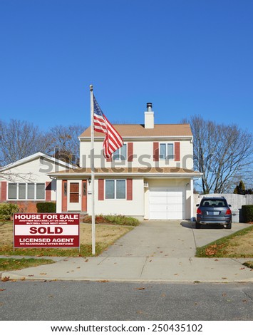 American flag pole Real estate sold (another success let us help you buy sell your next home) sign Suburban home burnt dry front yard lawn blue sky residential neighborhood autumn day USA