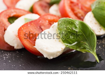 Caprese salad with mozzarella, tomato, basil and balsamic vinegar arranged on black plate 