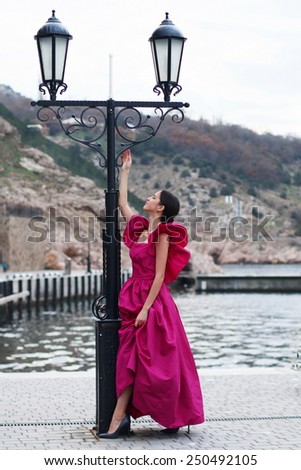Young woman in luxurious vintage pink dress staying on the embankment