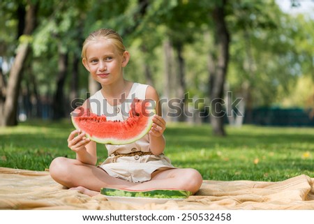 Cute girl sitting in park and eating watermelon