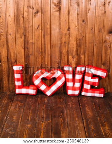 Love word of plush red letters on wood corner background. Full plaid textile. February 14, Valentine's Day concept shot with text space. Top view. High resolution