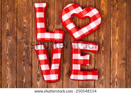 Love word of plush red letters on wood background. Full plaid textile. February 14, Valentine's Day concept shot with text space. Top view. High resolution