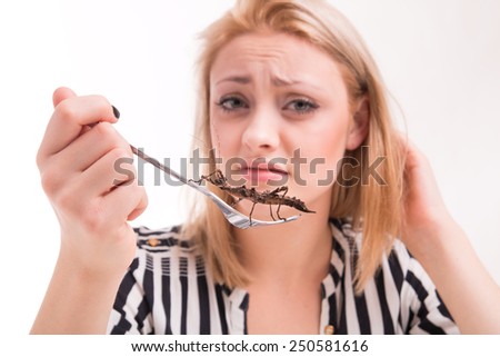 Disgusted woman eating big insects with a fork in a restaurant 
