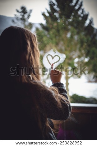 Closeup portrait of little girl drawing heart on frozen window