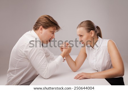 Man and woman in arm wrestling gesture on working table during meeting. Isolated over grey background.