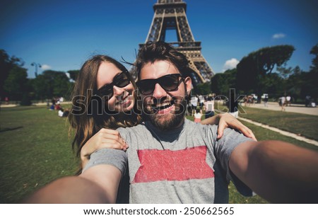 Happy smiling couple kissing and taking selfie photo in front of Eiffel Tower in Paris while traveling across France
