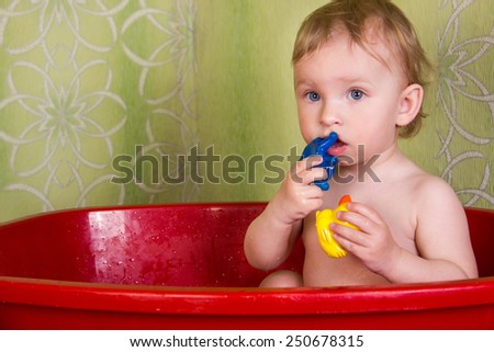 Beautiful little blond girl sitting in the bathroom and chew toys