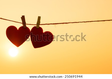 Love for Valentine's day - Two red hearts hung on the rope together with sunset silhouette Royalty-Free Stock Photo #250691944