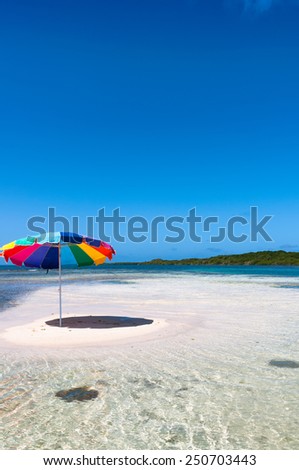Tropical white sand island beach with umbrella and a deep blue cloudy sky
