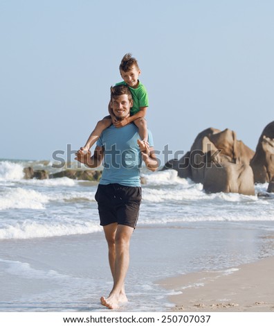 happy family on beach playing, father with son walking sea coast, rocks behind smiling