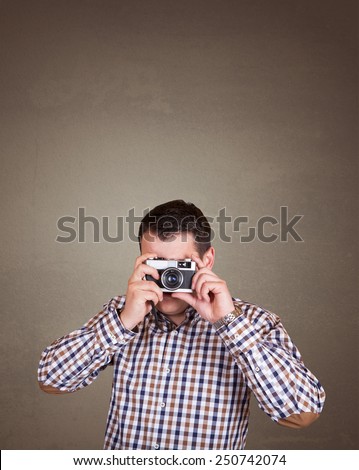 Young and handsome photographer man taking a picture with old retro (vintage) camera on old brown wall background with place for your text or drawing