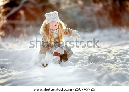 little girl sitting on snow and playing in winter