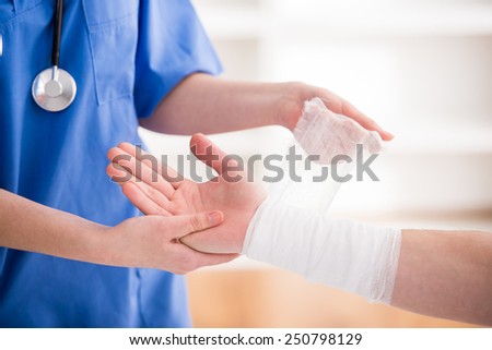 Close-up female doctor is bandaging upper limb of patient. Royalty-Free Stock Photo #250798129