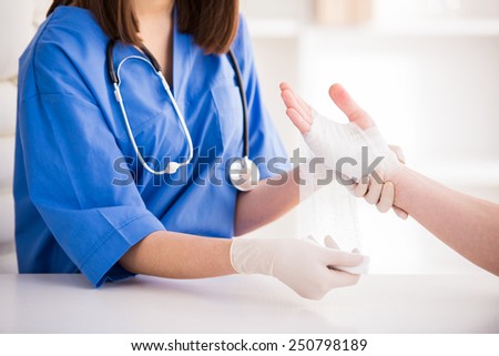 Close-up female doctor is bandaging upper limb of patient. Royalty-Free Stock Photo #250798189