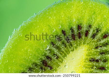 Kiwi fruit in water with bubbles over green background.