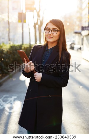 Portrait of attractive businesswoman standing outdoors at sunny evening and holding a digital tablet