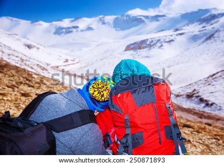 Happy couple, travelers enjoying snowy view, sitting on top of the mountain, romantic extreme winter vacation, active lifestyle