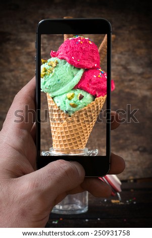 Ice cream with pistachios and strawberry in the cone photographing by phone camera