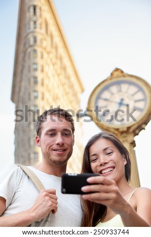 Travel couple taking selfie in New York City NYC, USA. Tourists holding smartphone to photograph self-portrait in front of famous Flatiron building downtown in summer.