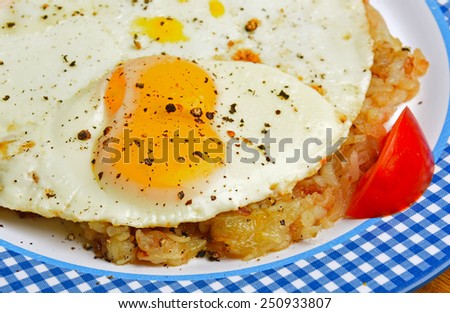 Close up of seasoned fried eggs served over hash brown potatoes with sliced tomato garnish on blue checkered plate