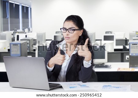 Young female indian manager working with laptop and showing thumbs up in the office