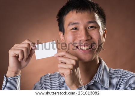 Young Chinese frank businessman holding blank white business card, closeup portrait in studio.