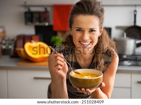 Happy young woman eating pumpkin soup in kitchen Royalty-Free Stock Photo #251028409