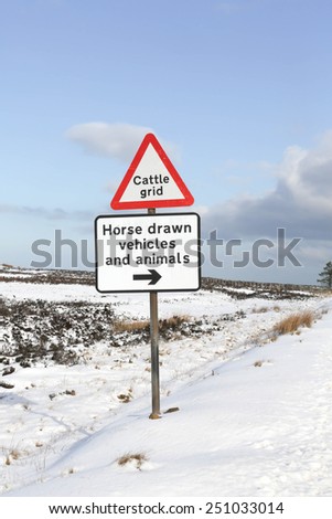 Red and white triangular warning road sign indicating a 'Cattle Grid' ahead in wintry conditions
