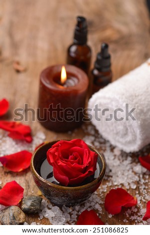 roses in bowl with pile of salt ,stones ,oil,towel,candle on old wooden board