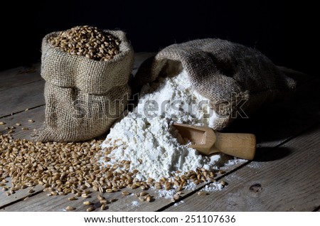Jute Bags Filled with Wheat and Flour on an Old Wooden Table Over Black Background Royalty-Free Stock Photo #251107636