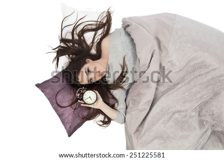 Beautiful woman holding an alarm clock while laying in bed against a white background