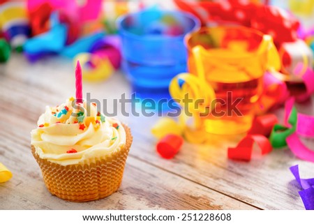 Celebrating a special day. Side view image of a cupcake with multicolored confetti as a frame and bright glasses on the background