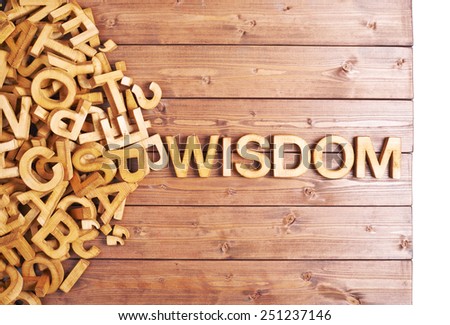 Word wisdom made with block wooden letters next to a pile of other letters over the wooden board surface composition