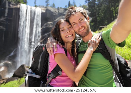 Selfie couple hikers at Yosemite National Park taking a self portrait picture with beautiful waterfall, Vernal Fall. Young hiking couple relaxing after hike in beautiful summer nature landscape.