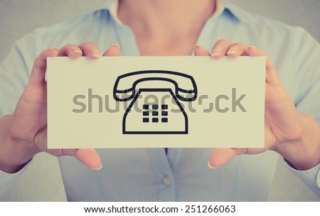Closeup businesswoman hands holding white card sign with telephone contact icon isolated on grey wall office background. Retro instagram style image