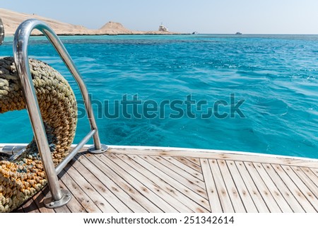 Close-up of a wooden deck end of a yacht and island on background Royalty-Free Stock Photo #251342614