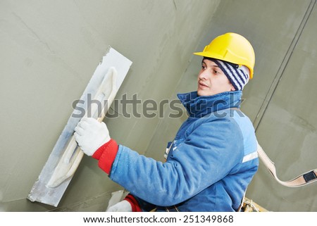 builder at facade plastering work during industrial building with putty knife float