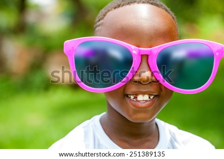 Close up face shot portrait of cute African boy wearing huge over sized sun glasses outdoors. Royalty-Free Stock Photo #251389135