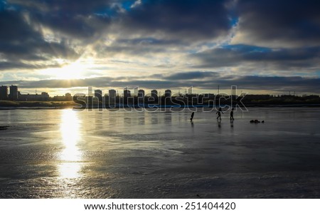 The children play on the skate on the ice Bay at sunset against the backdrop of the city