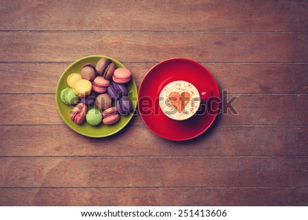 Cup of Cappuccino with heart shape symbol and macarons on wooden background