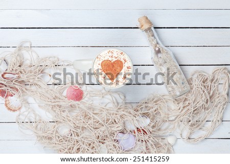 Cup of Cappuccino with heart shape symbol and net with bottle on white wooden background